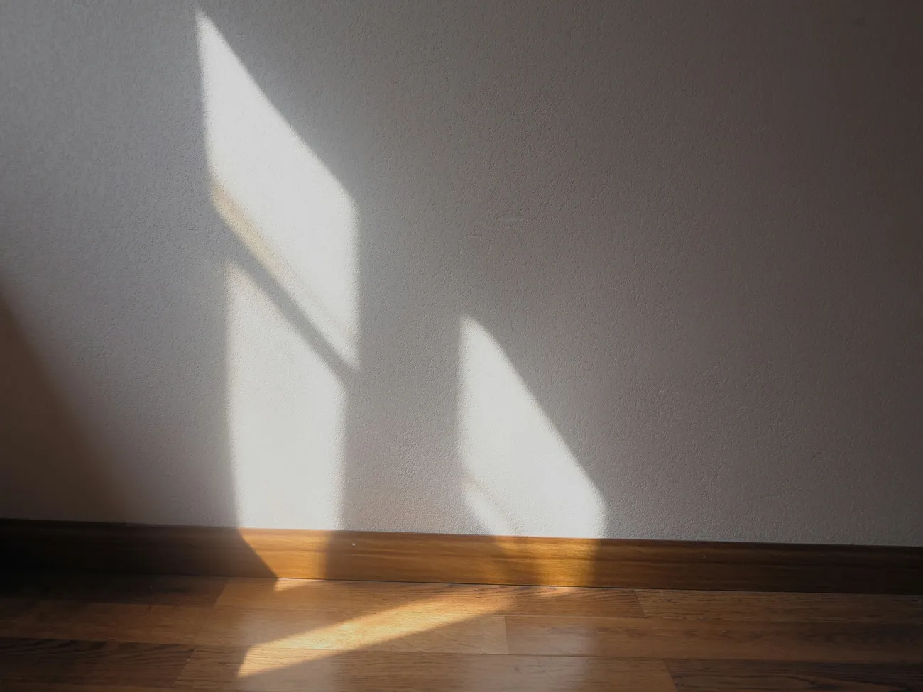 Luz de una ventana sobre una pared blanca y un suelo de madera